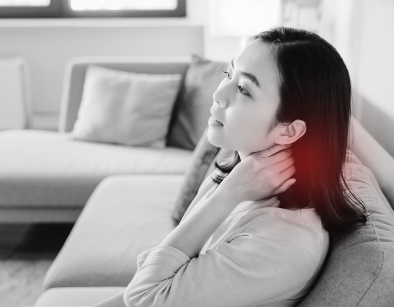 事故後数日してから首の違和感に気づいた女性が、自宅のソファで首を軽く押さえている様子