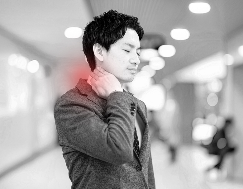 交通事故後、仕事復帰したものの首の違和感が続き、駅構内で首をそっと押さえる男性の様子